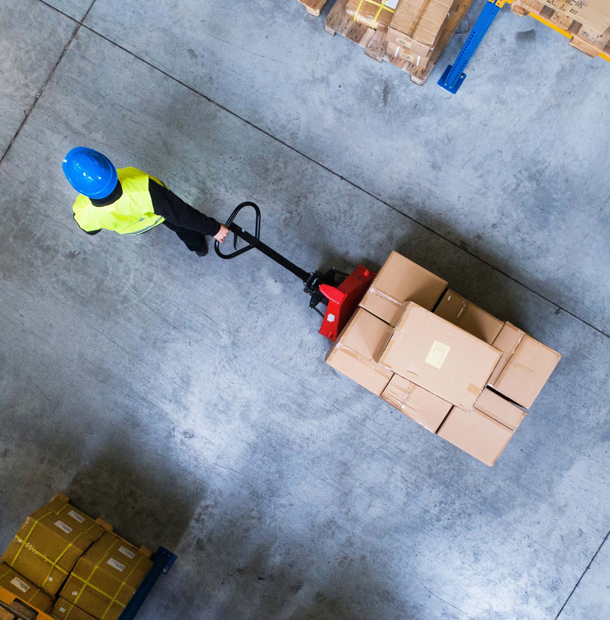 an aerial view of a warehouse worker pulling a dolly of boxes between two aisles